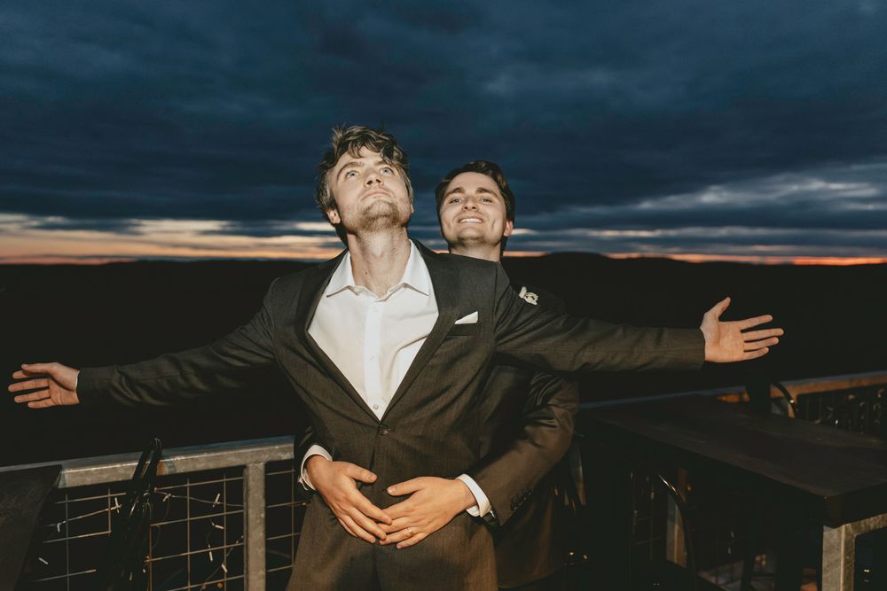 Two people pose dramatically against a moody sunset sky on an outdoor deck.