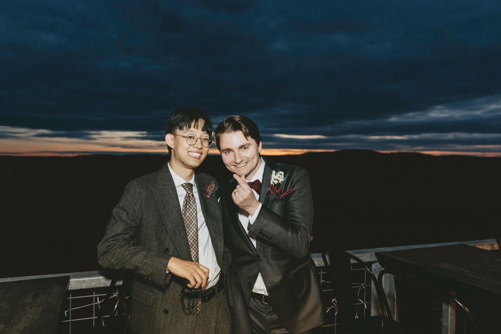 Two friends posing together against a dramatic sunset sky at an outdoor event.