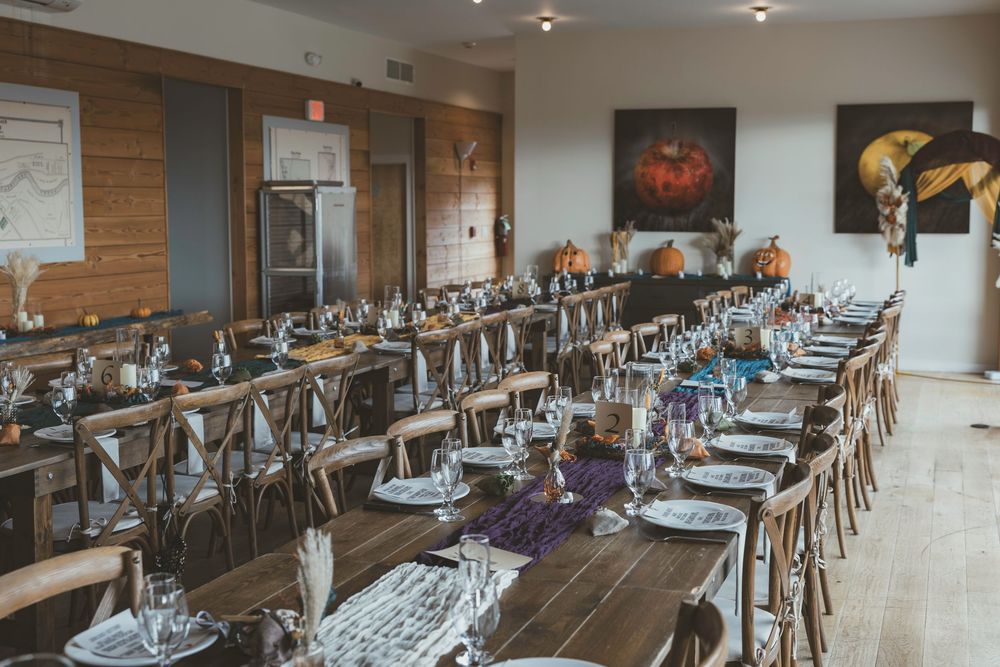Long banquet tables with elegant place settings and wooden chairs line a modern restaurant dining room with brick walls.