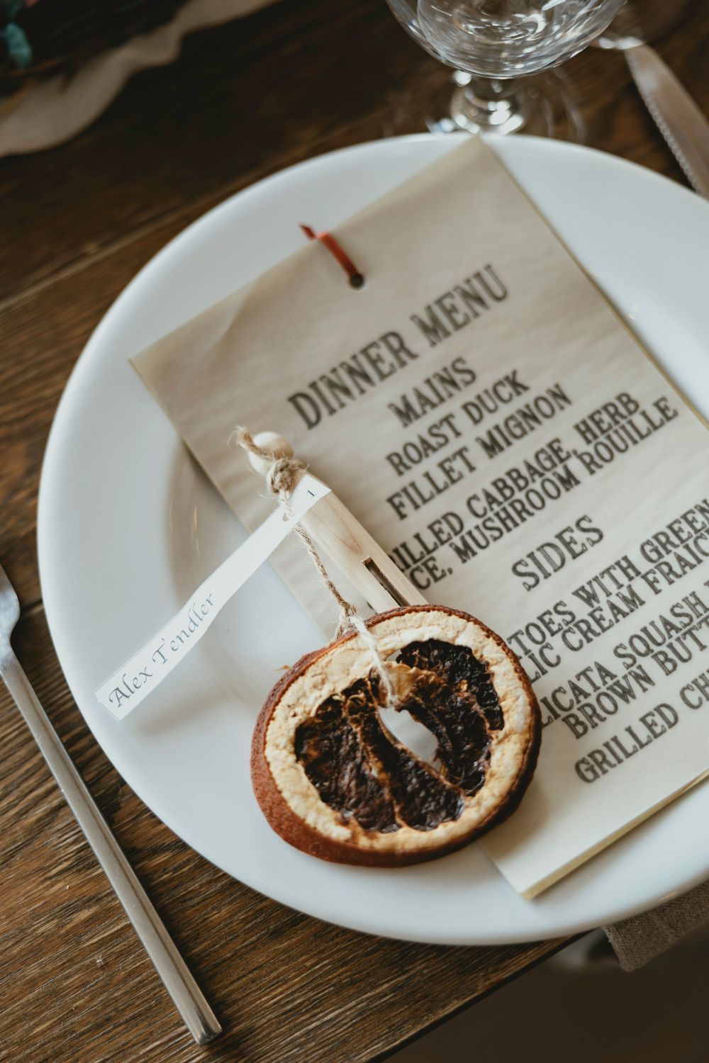 Close-up view of menu cards and burnt orange citrus garnishes on white plates at an elegant dinner setting.