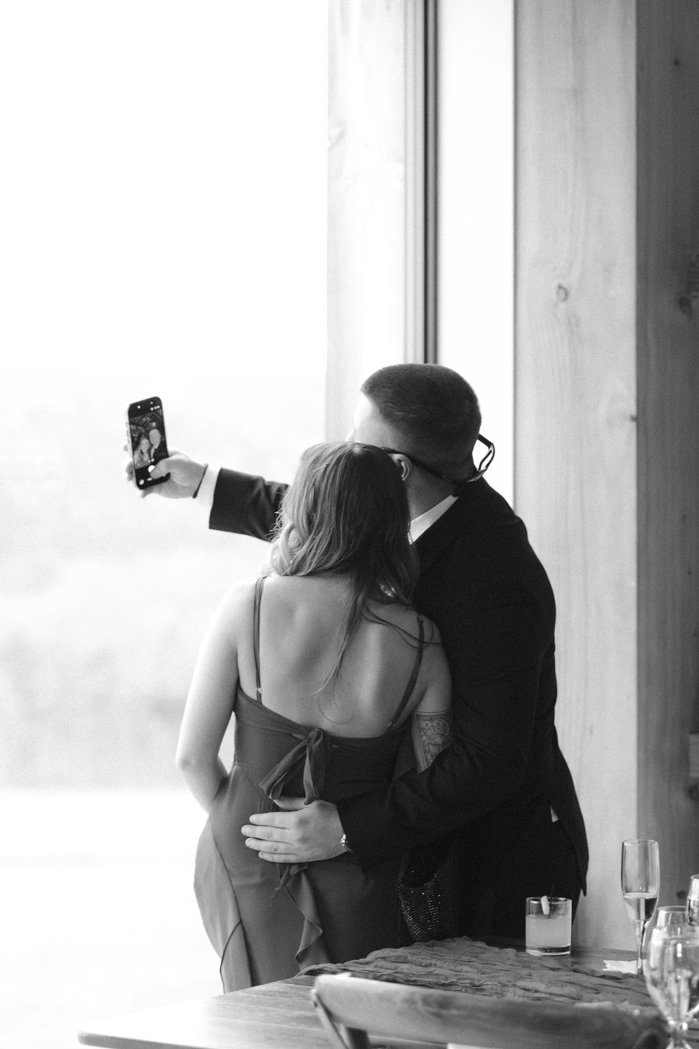 A couple in silhouette embraces intimately against a bright window background in a romantic black and white photograph.