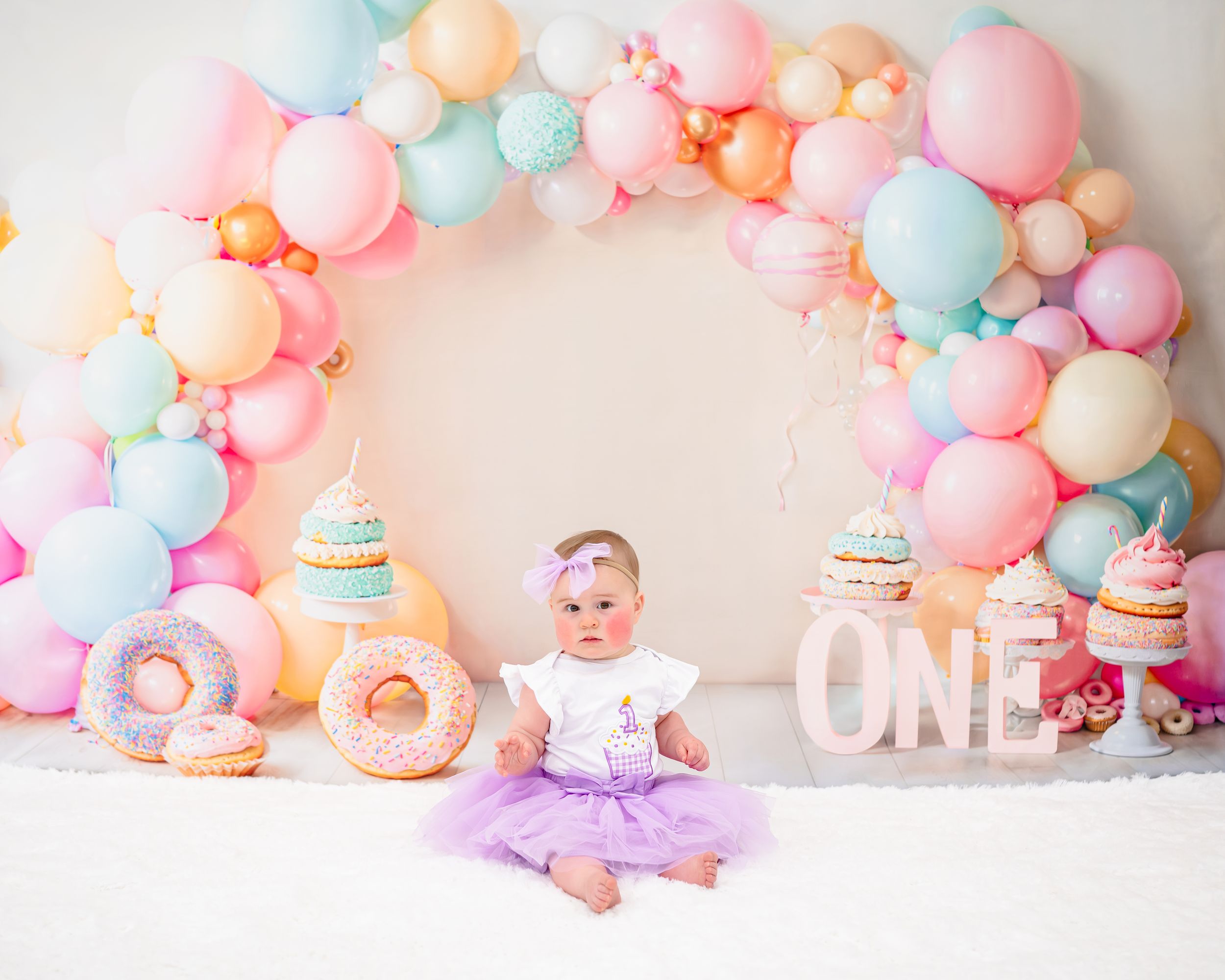 A series of pastel balloon decorations with pink, blue, and white colors arranged for a first birthday celebration.