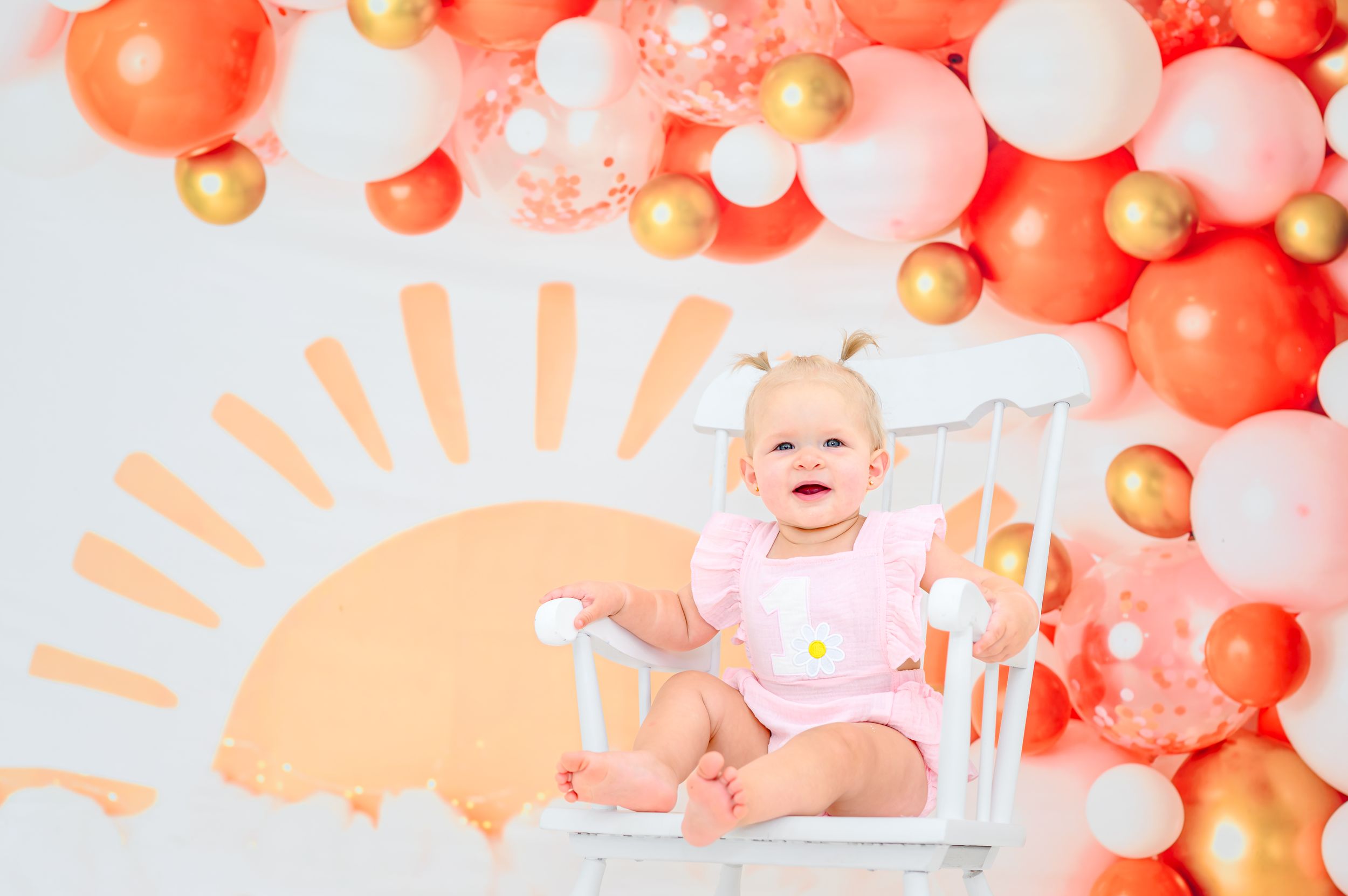 A festive party setup with pink and coral balloon garlands and decorative elements against a white backdrop.