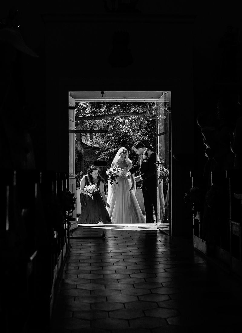 French chateau wedding ceremony moment with bride and groom standing in doorway framed by soft light, captured in a timeless black and white