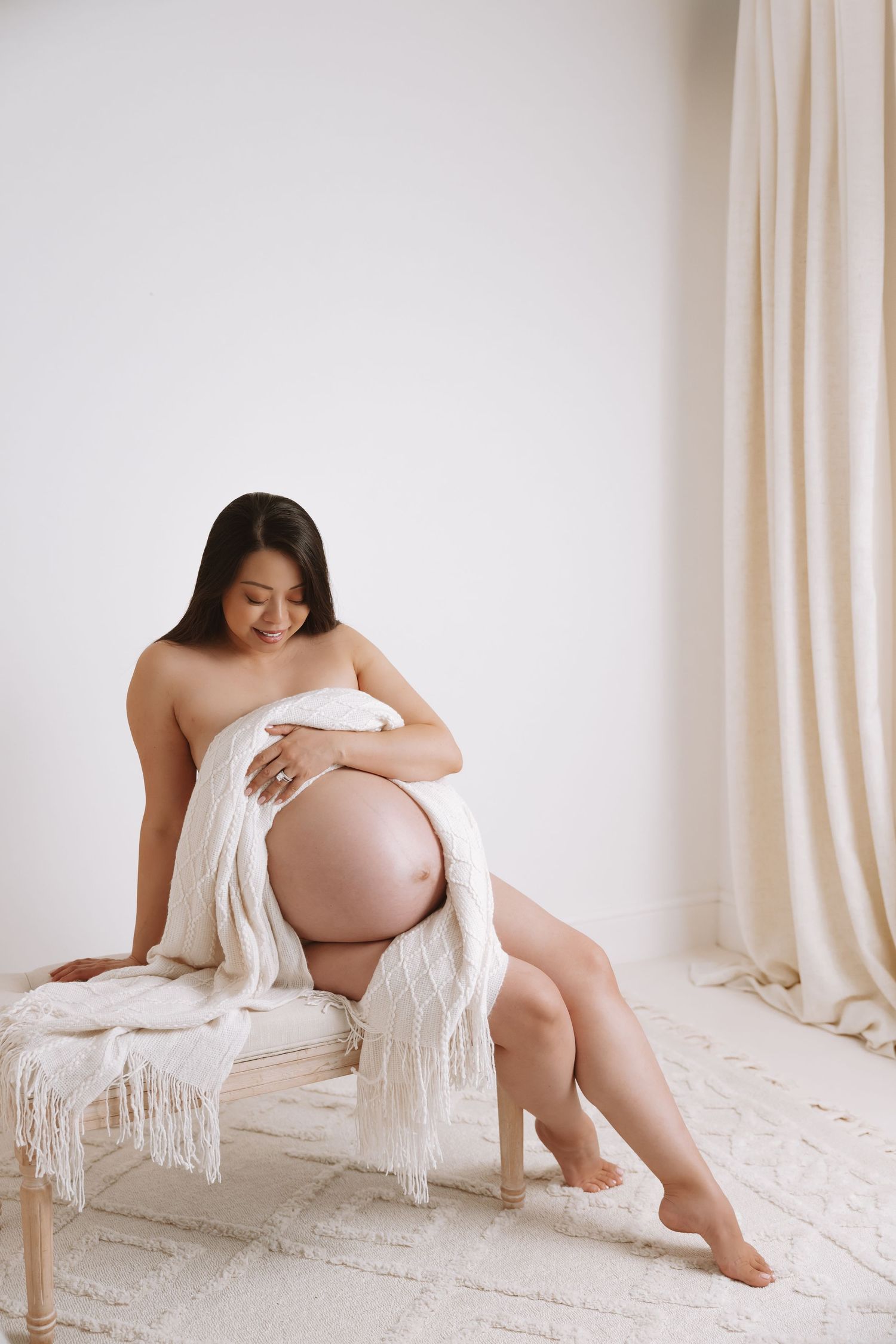 Artistic maternity photo series showing a pregnant woman draped in white fabric against light curtains.