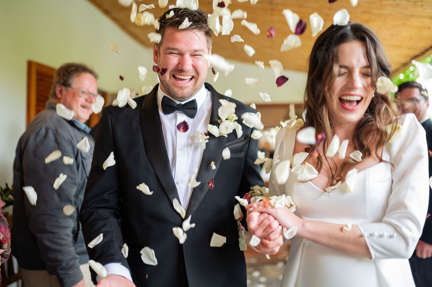 Joyful bride and groom laughing as colorful confetti falls during their wedding ceremony exit.