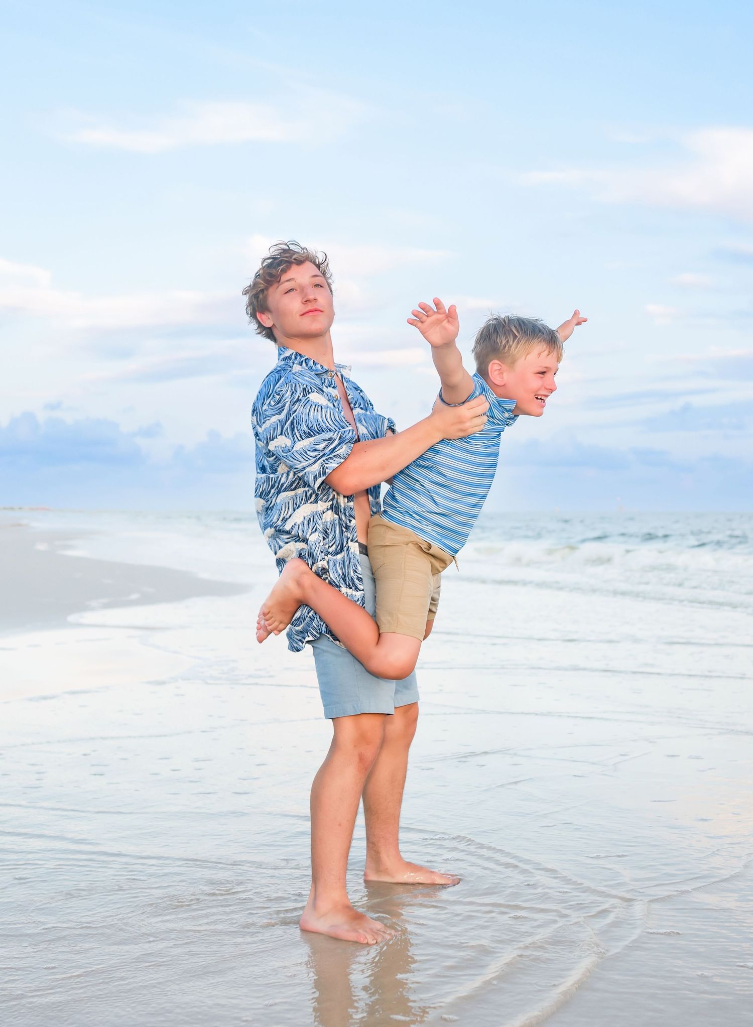 Older brother holding his younger sibling during a playful Dauphin Island beach photography session along the Alabama Gulf Coast.