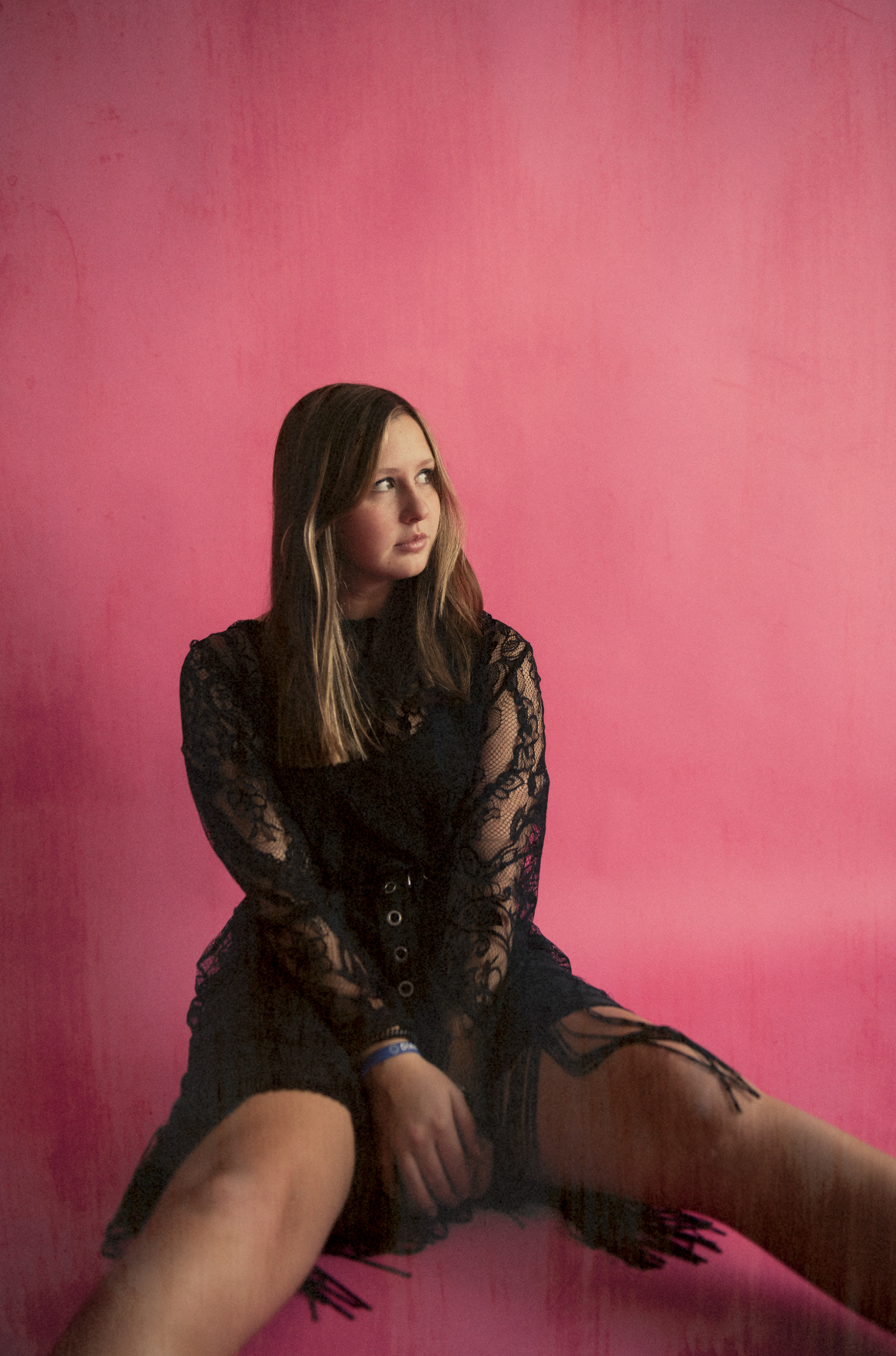 A figure in a black lace dress poses against a pink backdrop in an artistic fashion photo series.