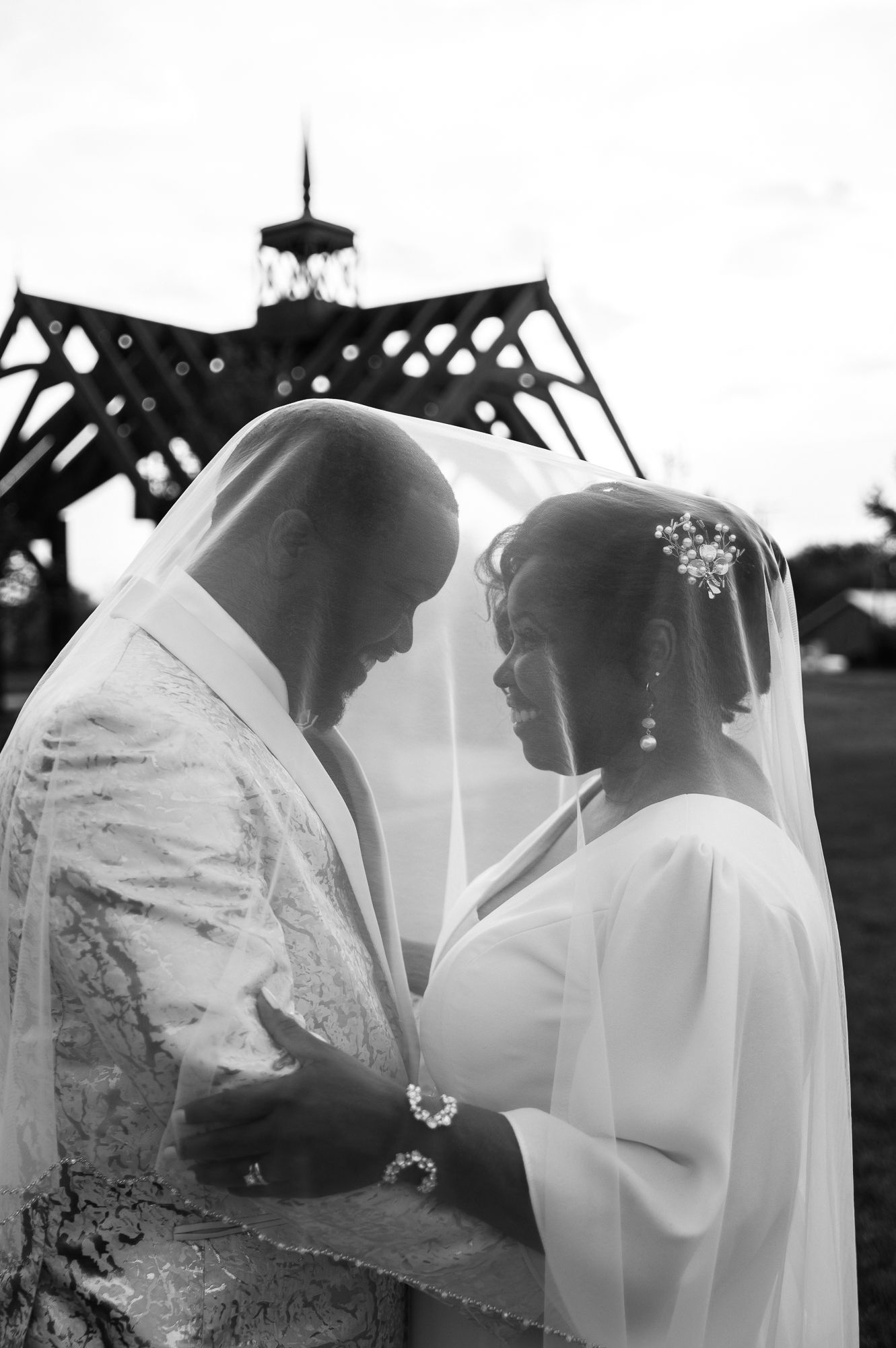 Black and white photo of a bride and groom sharing an intimate moment under a veil at their wedding ceremony.