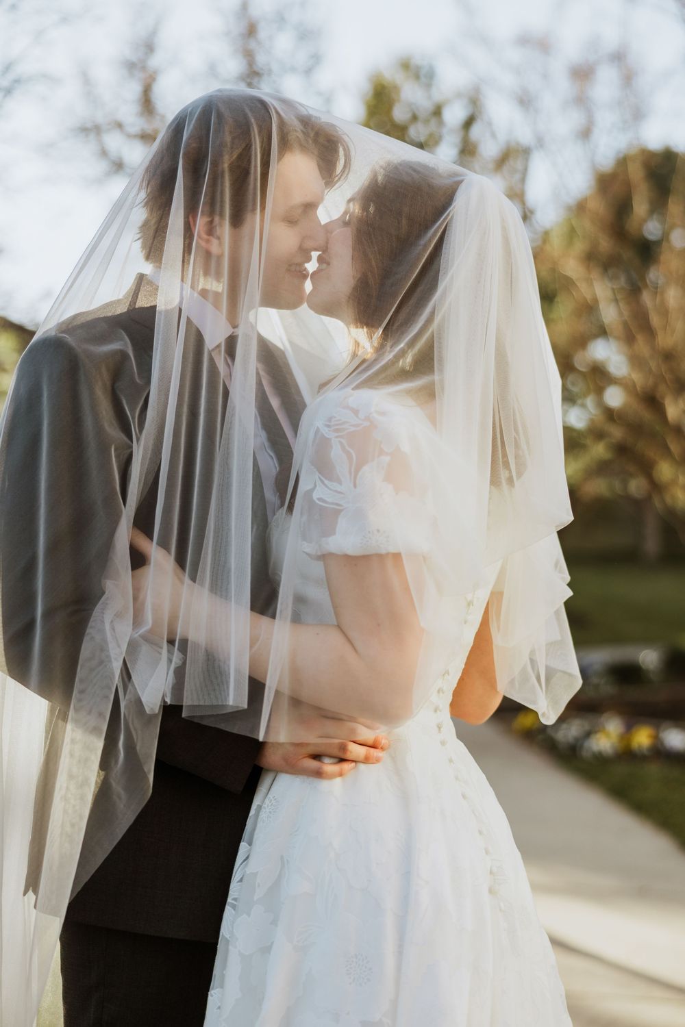 A husband and wife take bridal portraits, they are under her veil about to kiss