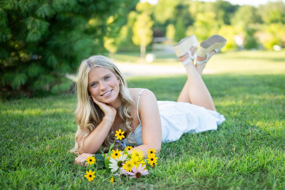 A person in a white dress lies in green grass with yellow flowers on a sunny summer day.