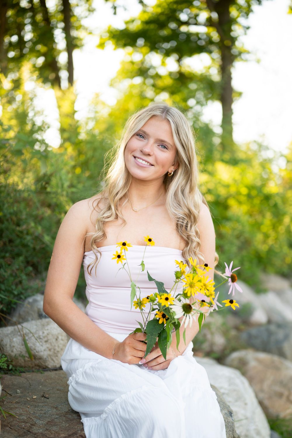 A bride in a white dress holds a cheerful bouquet of yellow wildflowers while posing outdoors in golden sunlight.