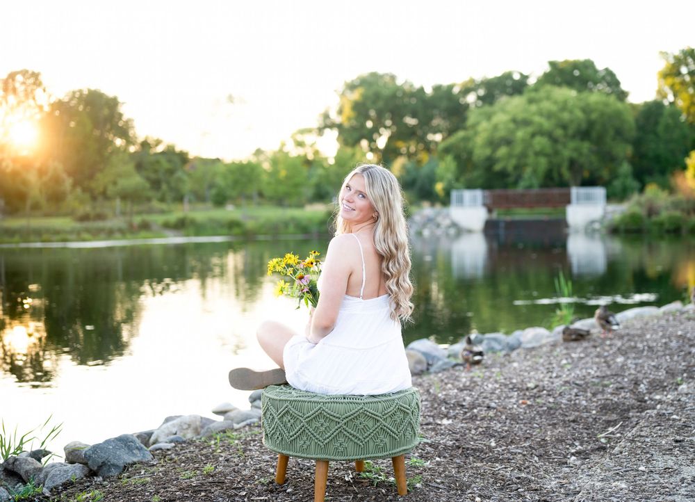 A romantic lakeside engagement photo session at sunset with a couple sitting on a rustic wooden bench by the water.