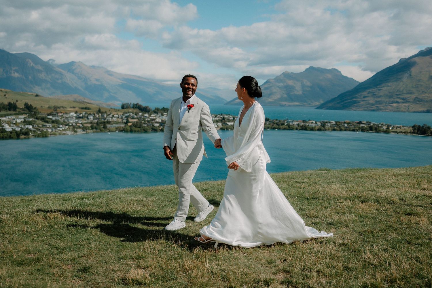 A newly married wedding couple walks through scenic mountain landscapes overlooking pristine Lake Wakatipu, Queenstown, New Zealand.