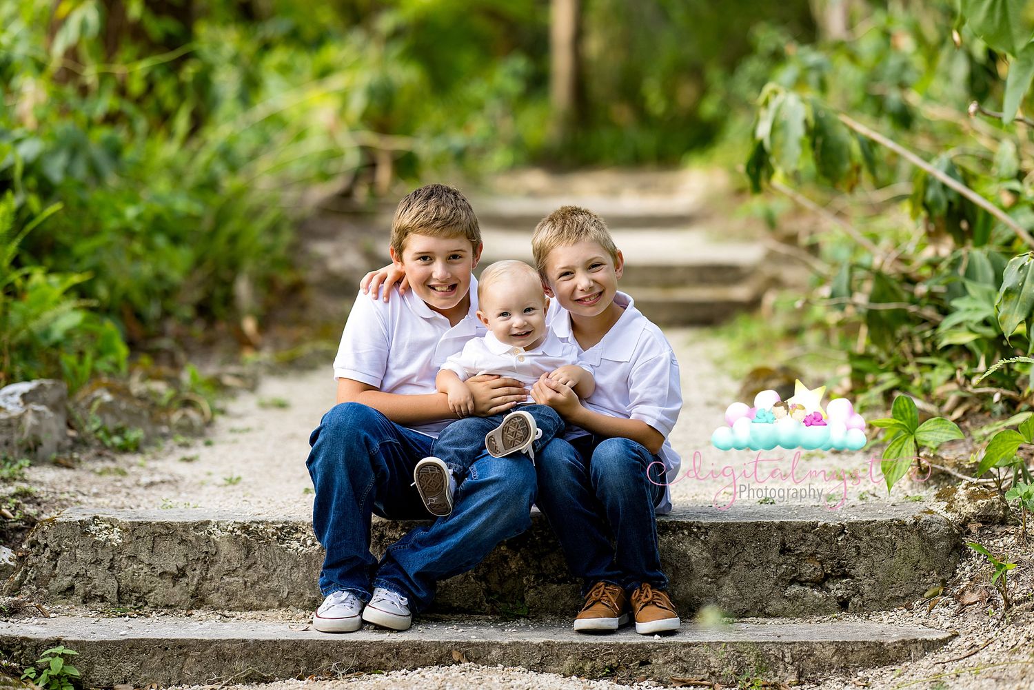 Family sitting together on outdoor stone steps surrounded by green foliage on a sunny day.