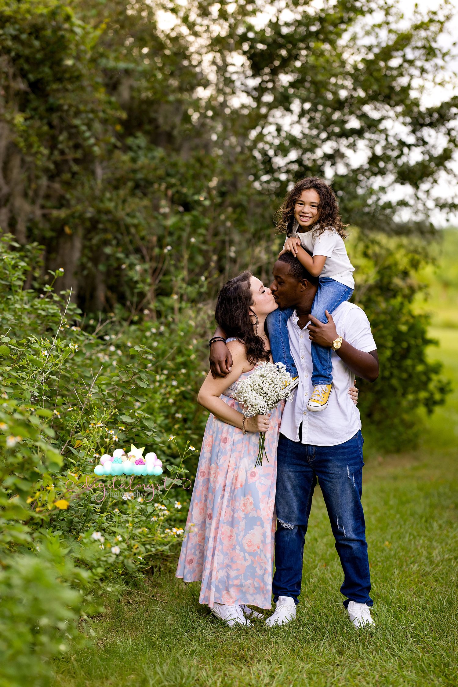 A couple embraces in a romantic outdoor garden setting with wildflowers and greenery surrounding them.
