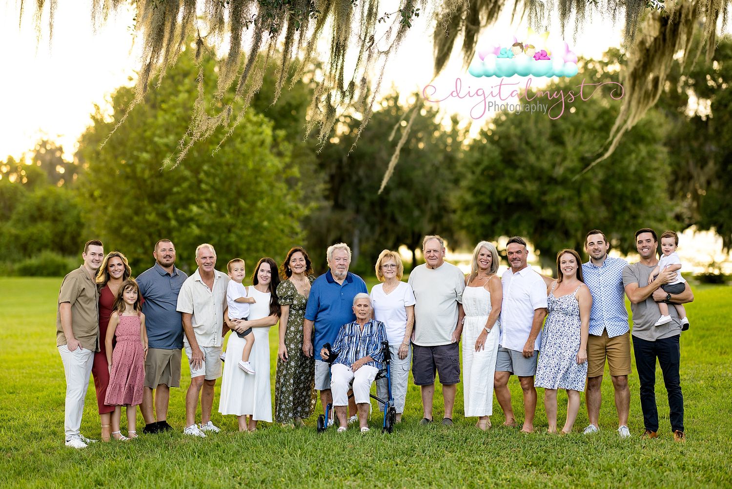 A large family group poses together outdoors on a lawn with Spanish moss draped trees in the background.