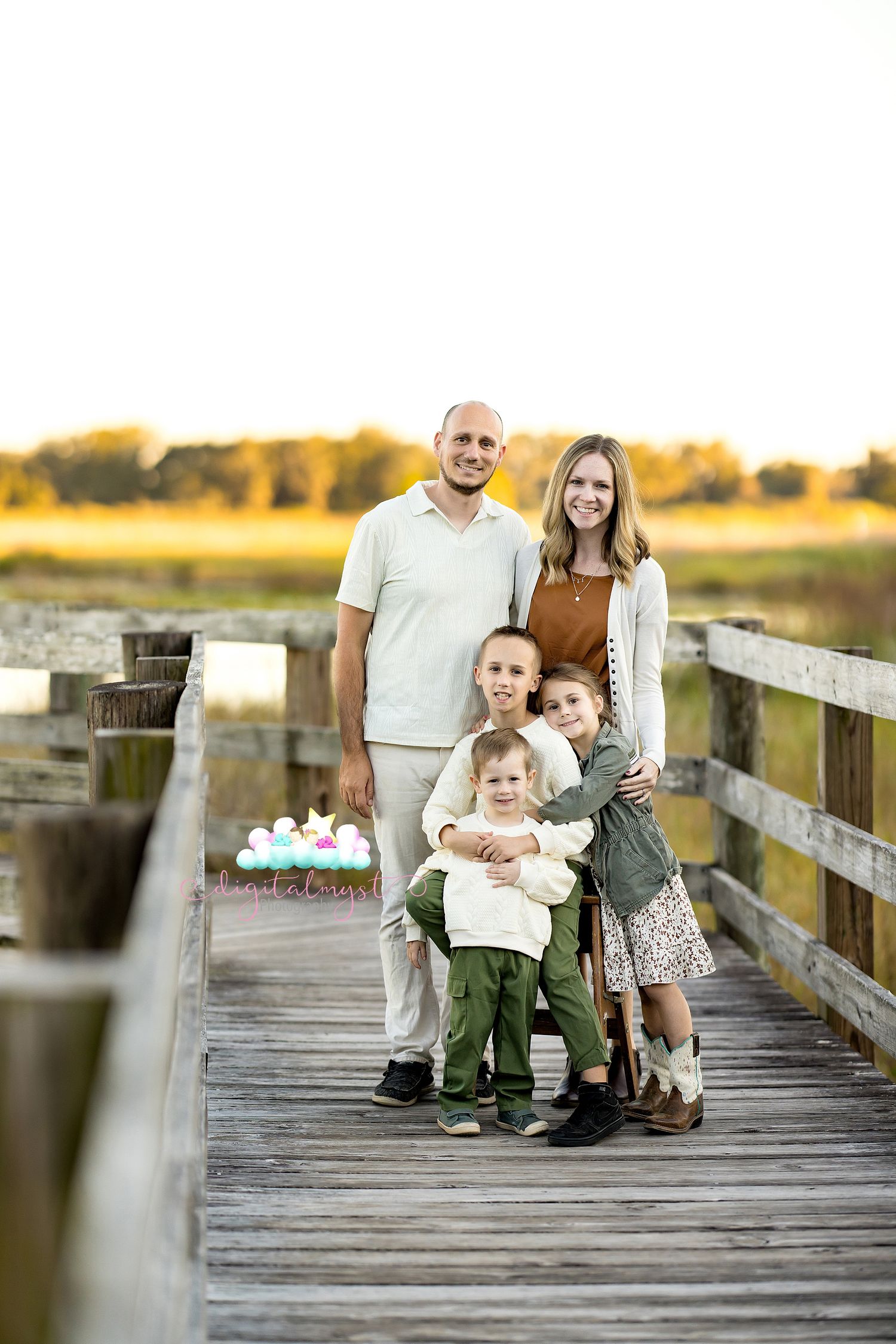 Family sitting together on a wooden boardwalk at sunset with golden light in the background.