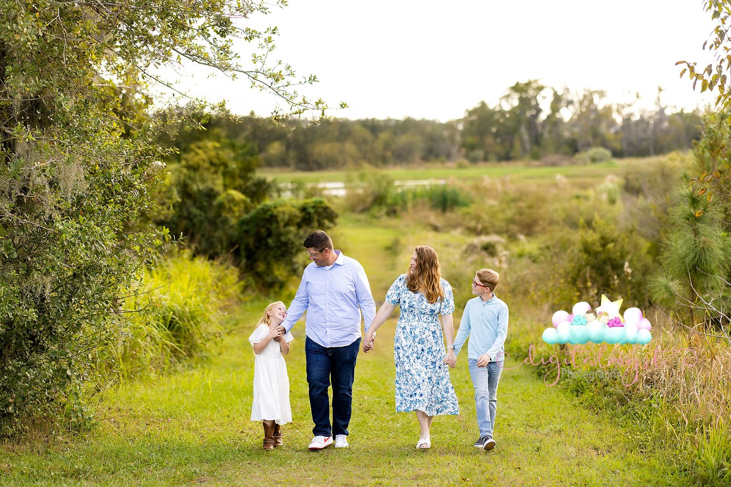 A family in coordinated blue and white outfits walking together through a sunny outdoor path in nature.