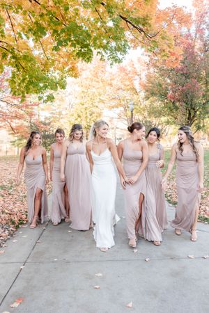 Wedding party in blush pink dresses walking together under beautiful fall foliage.