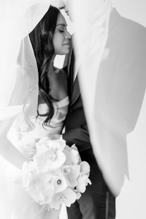 Black and white portrait of a bride with long dark hair and veil holding white flowers.
