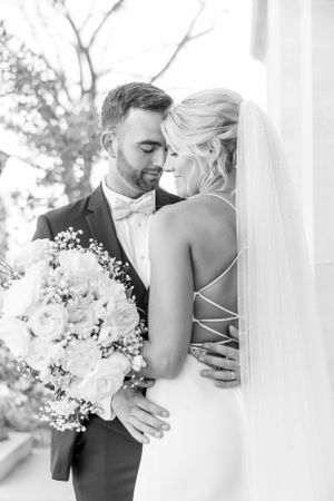 Intimate black and white portrait of couple sharing romantic moment with bridal bouquet.