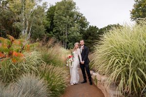 A couple walks along a garden path surrounded by tall ornamental grasses and autumn foliage.