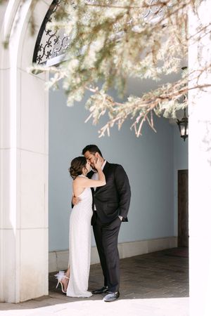 Bride and groom sharing a romantic kiss under blooming branches at an elegant venue archway.