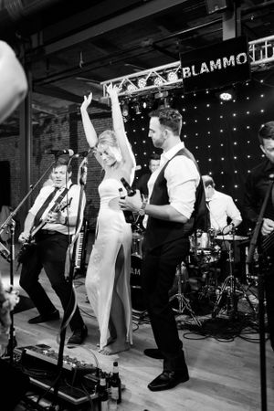 Black and white photo of wedding band performing on stage with energetic dancing at reception.