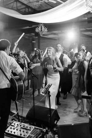 Black and white photo of wedding reception with live band and guests dancing under draped ceiling.