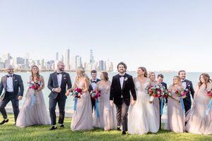 Wedding party walks by Chicago skyline, bridesmaids in blush gowns with pink bouquets, groomsmen in black tuxedos.