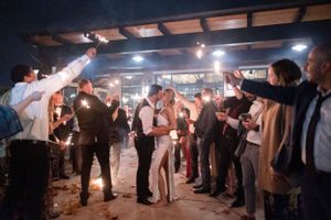 Wedding reception celebration with guests dancing under dimly lit wooden beams and string lights.