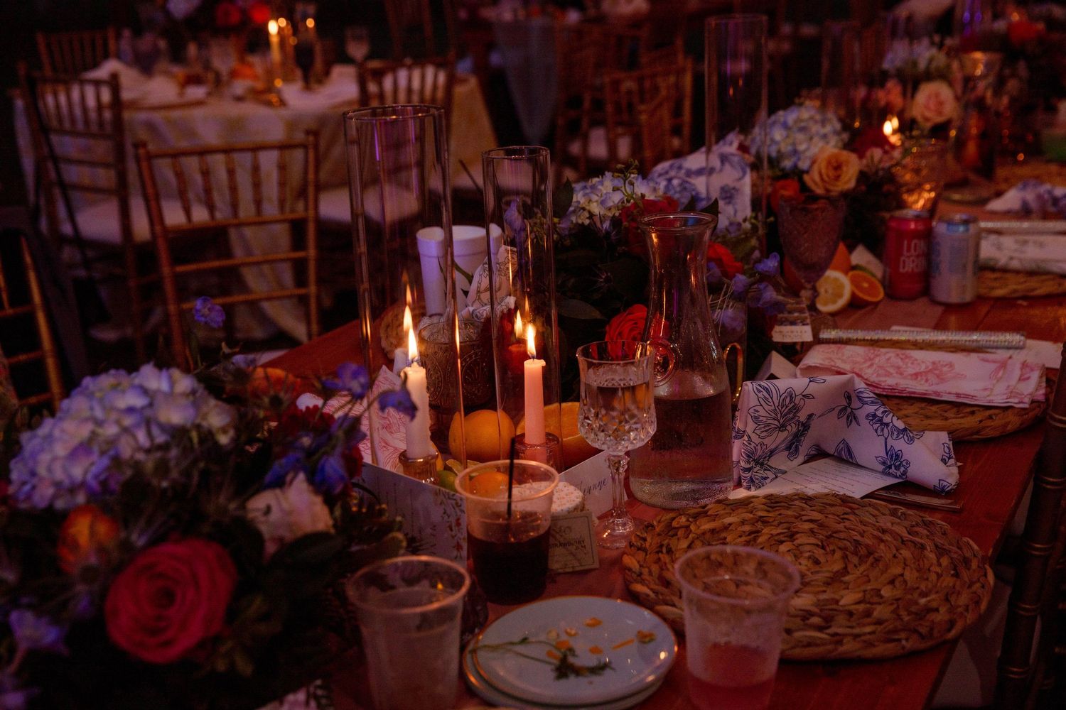 Elegant candlelit wedding reception table with floral centerpieces, hydrangeas, and decorative place settings in warm ambient lighting.