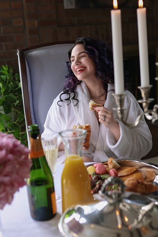 A person in white enjoys a meal at an elegant table setting with candles, drinks, and plates of food.