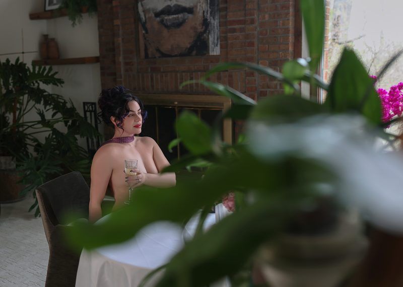 A person sits in a sunlit room with houseplants and brick walls, creating a cozy indoor garden atmosphere.