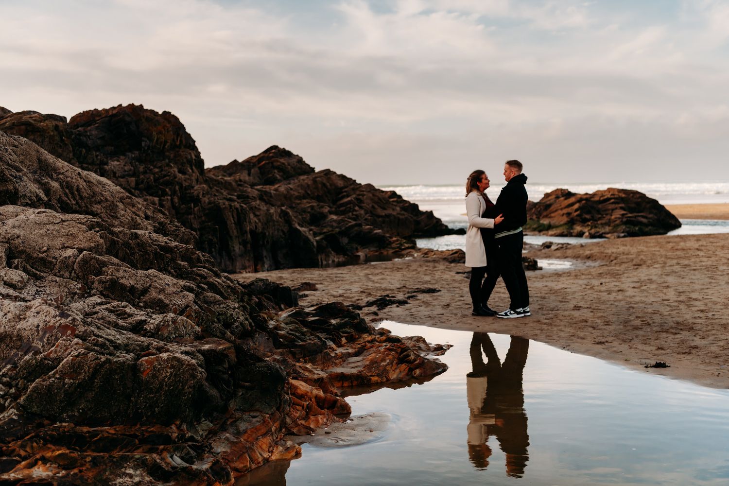 A couple walks along a scenic coastal path with dramatic cliffs and ocean views at sunset.