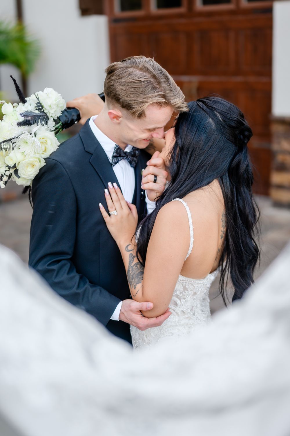 An intimate wedding moment captured as a couple shares a tender kiss against a light colored wall.