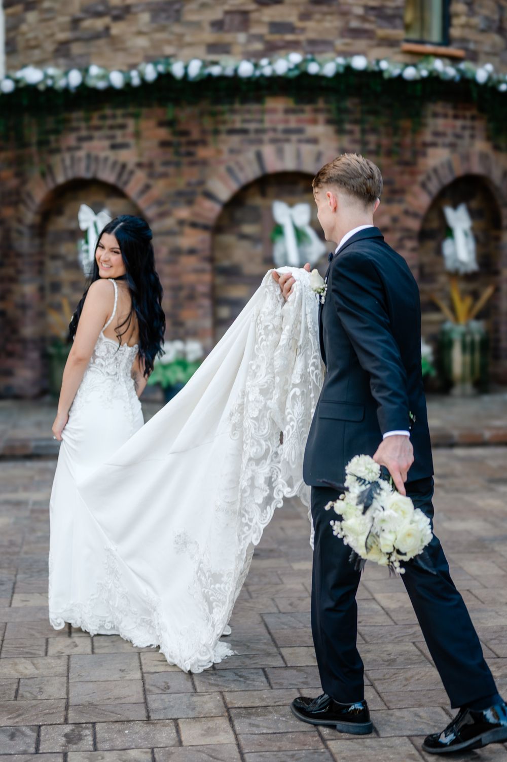 A series of wedding photos showing the train of a white lace dress and formal shoes against a brick backdrop.
