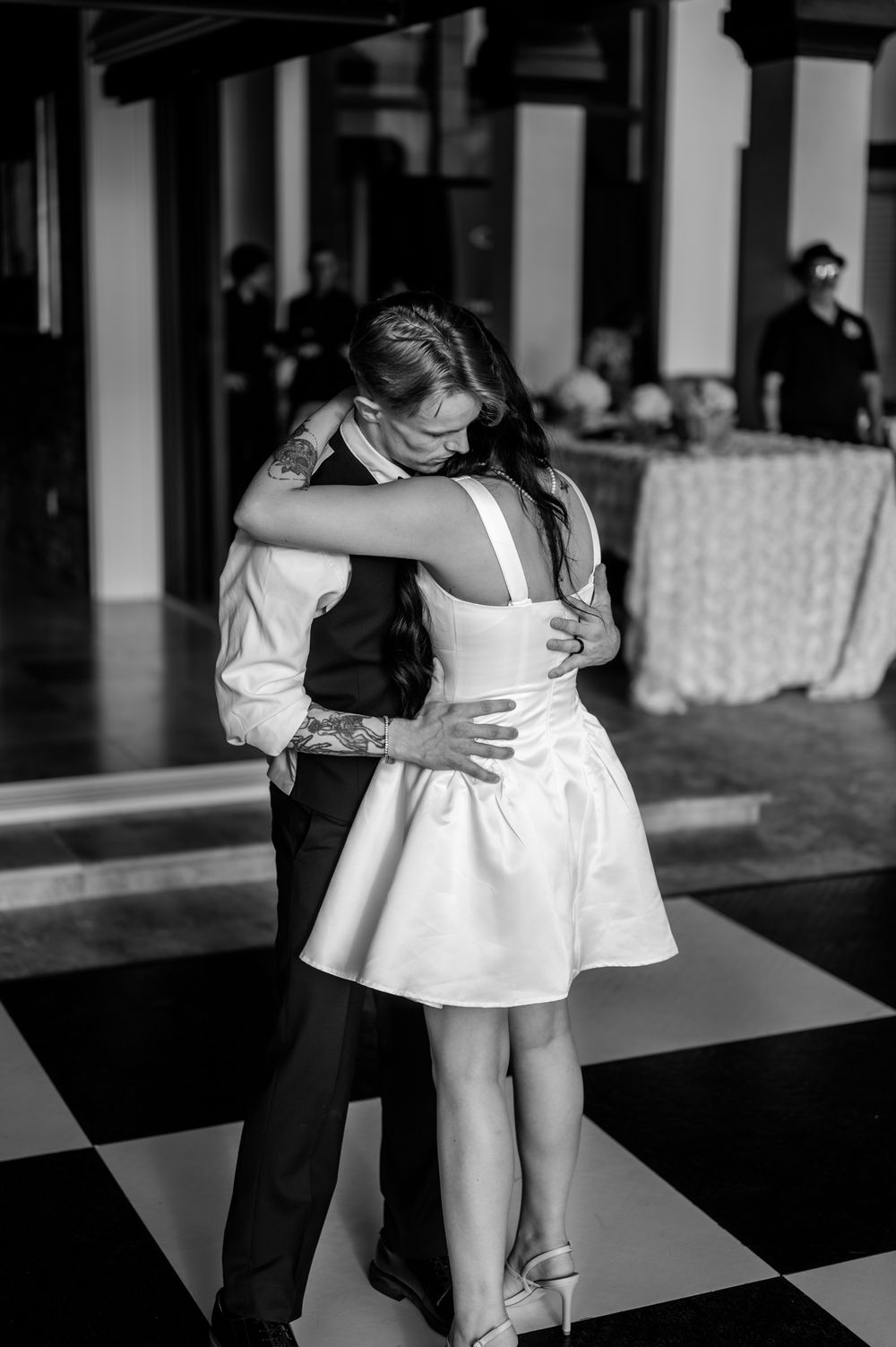 A couple dances intimately on a black and white checkered floor at their wedding reception.