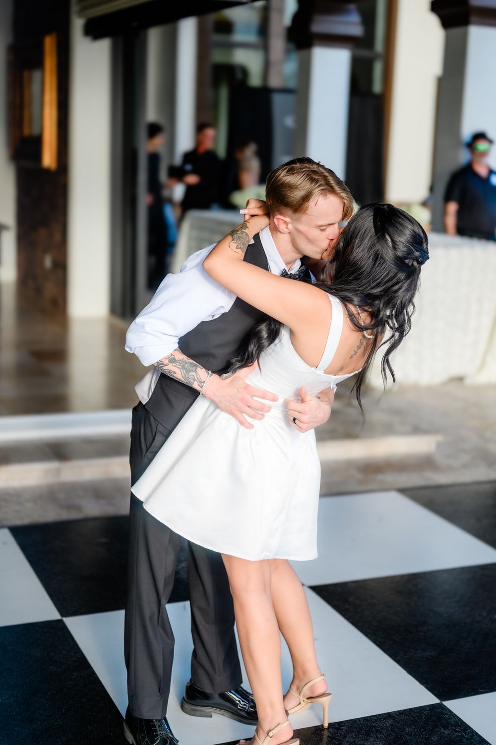 A romantic dip dance pose captured during a wedding celebration on a black and white checkered floor.