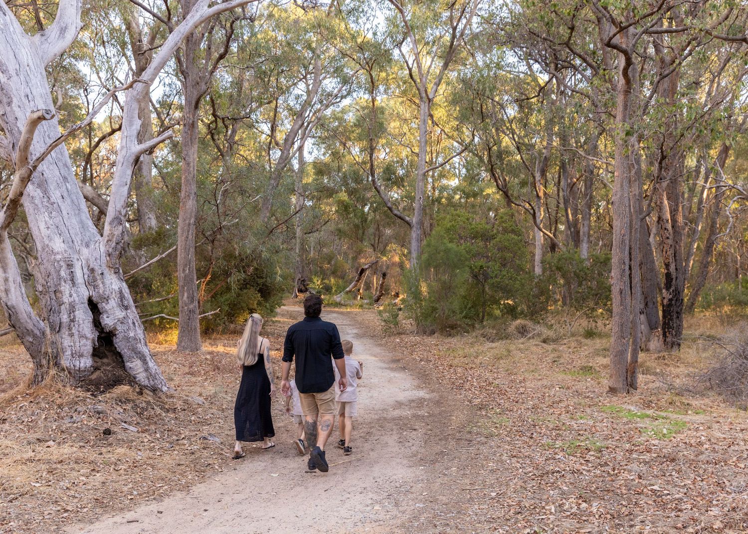 Unposed family photo of four walking on a dirt path through bushland, captured in a warm, natural style