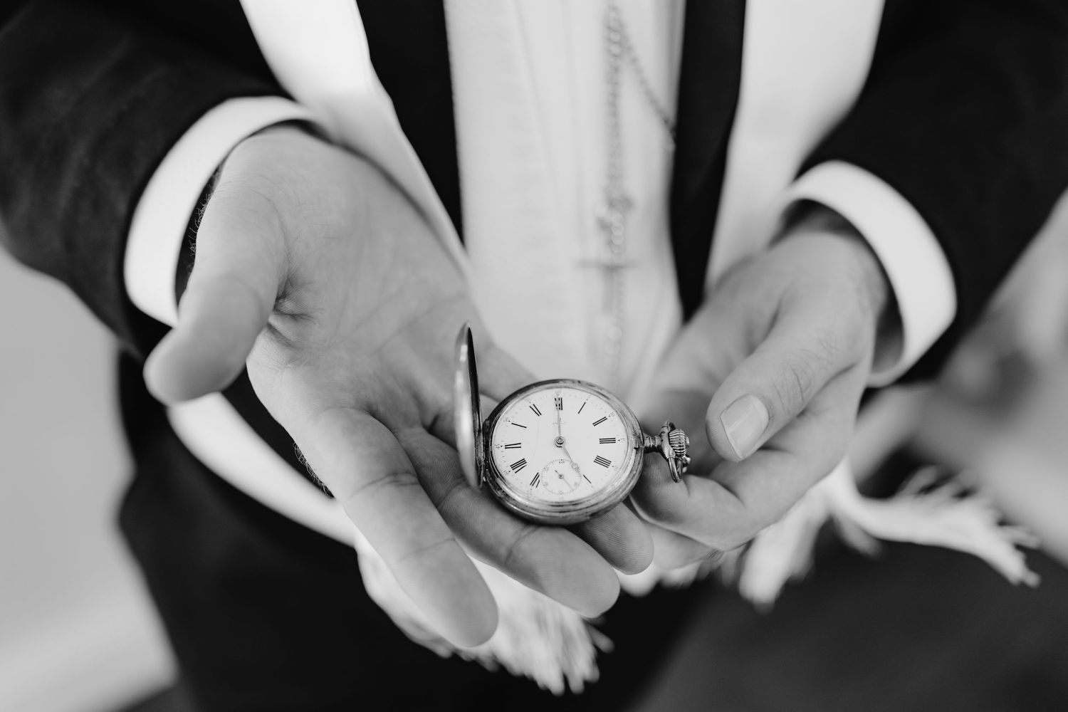 Close-up sequence of hands holding and manipulating a small pocket watch against a black and white background.