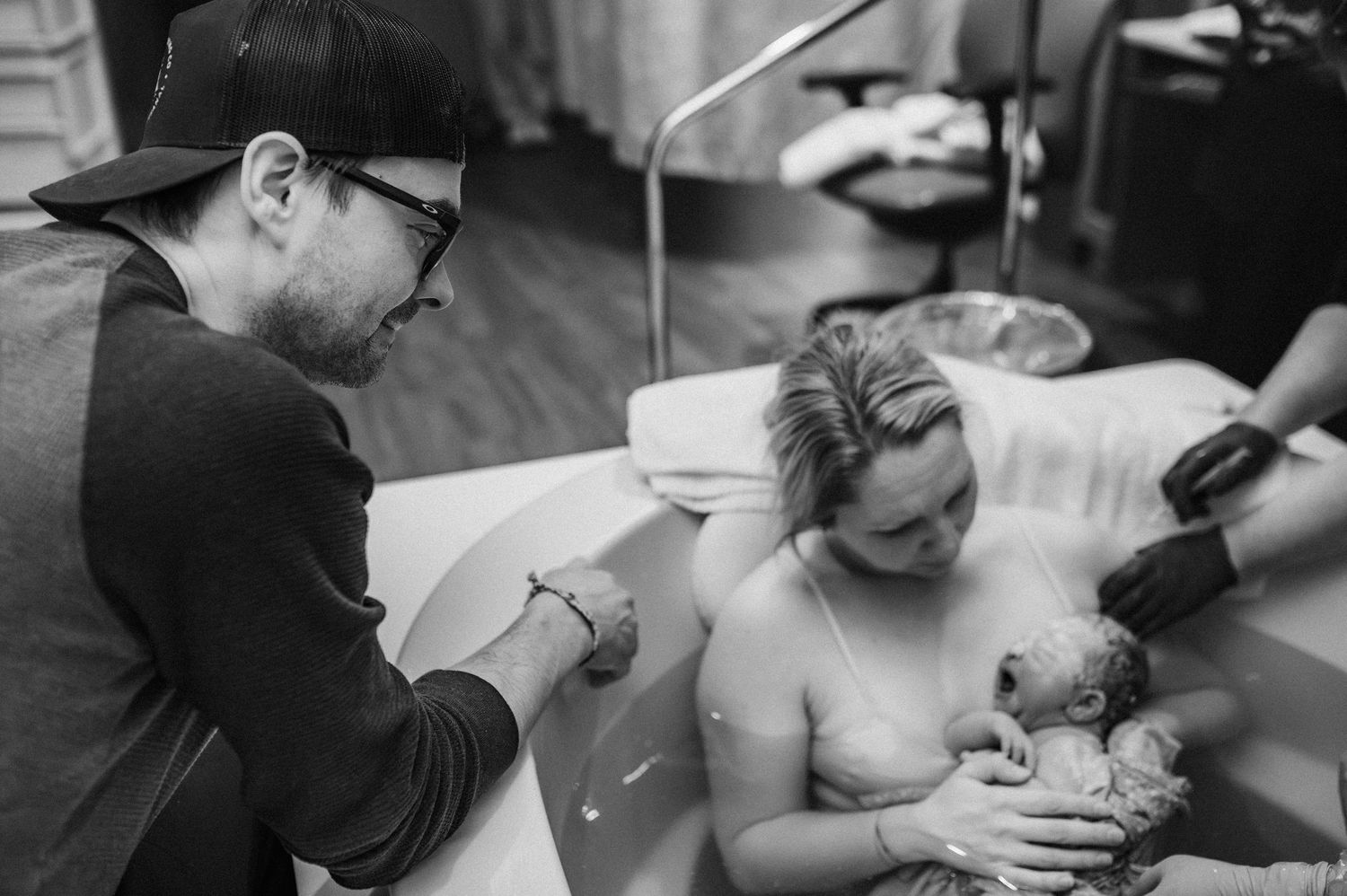 Black and white photograph showing a tattoo artist at work while client holds a small dog in a studio setting.
