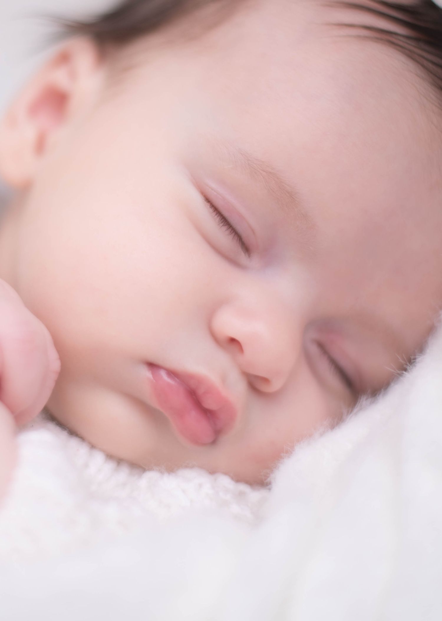 Close-up of a peacefully sleeping newborn baby with rosy lips resting on a soft white blanket.