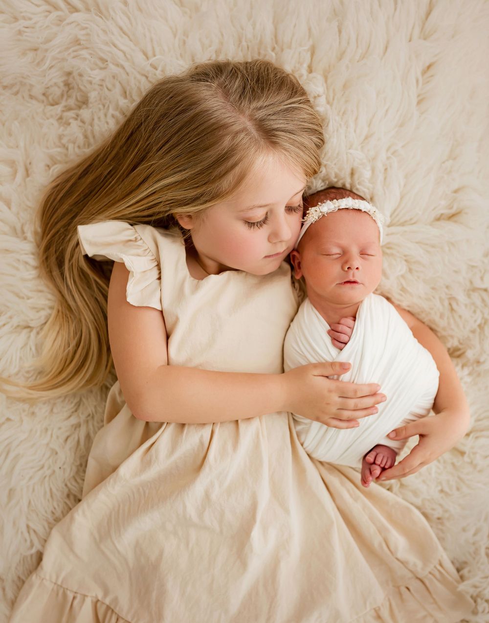 Big sister holding newborn baby on cream fur blanket during studio portrait session in Summerville SC