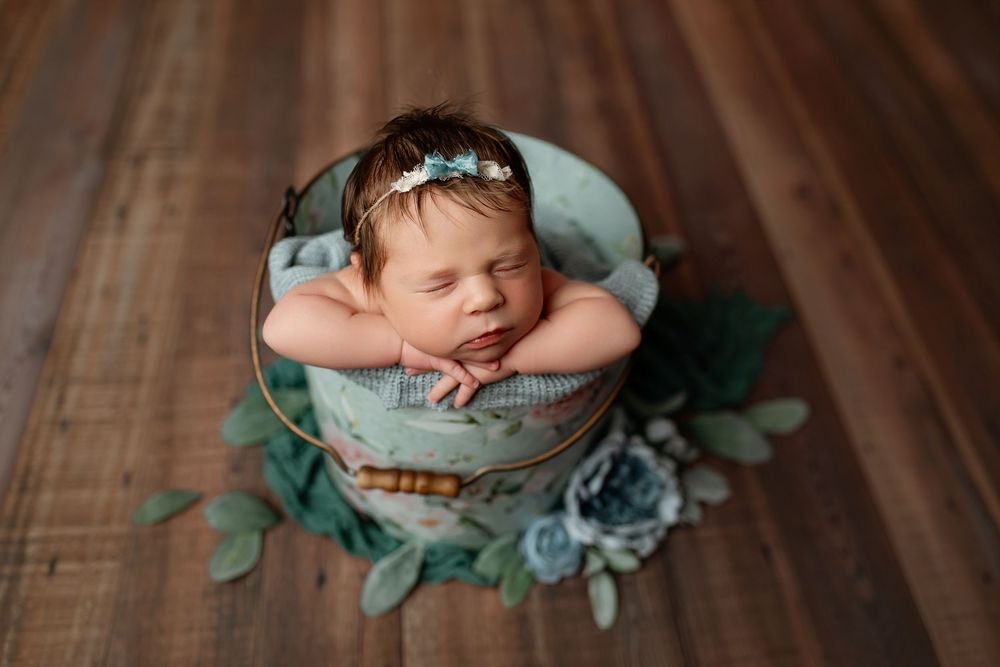 Newborn baby girl posed in floral bucket with sage greenery during Summerville SC studio session