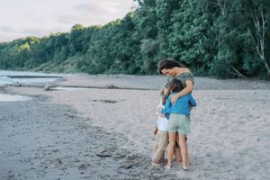 Small group strolling on a sandy beach with dense coastal forest visible along the shoreline.