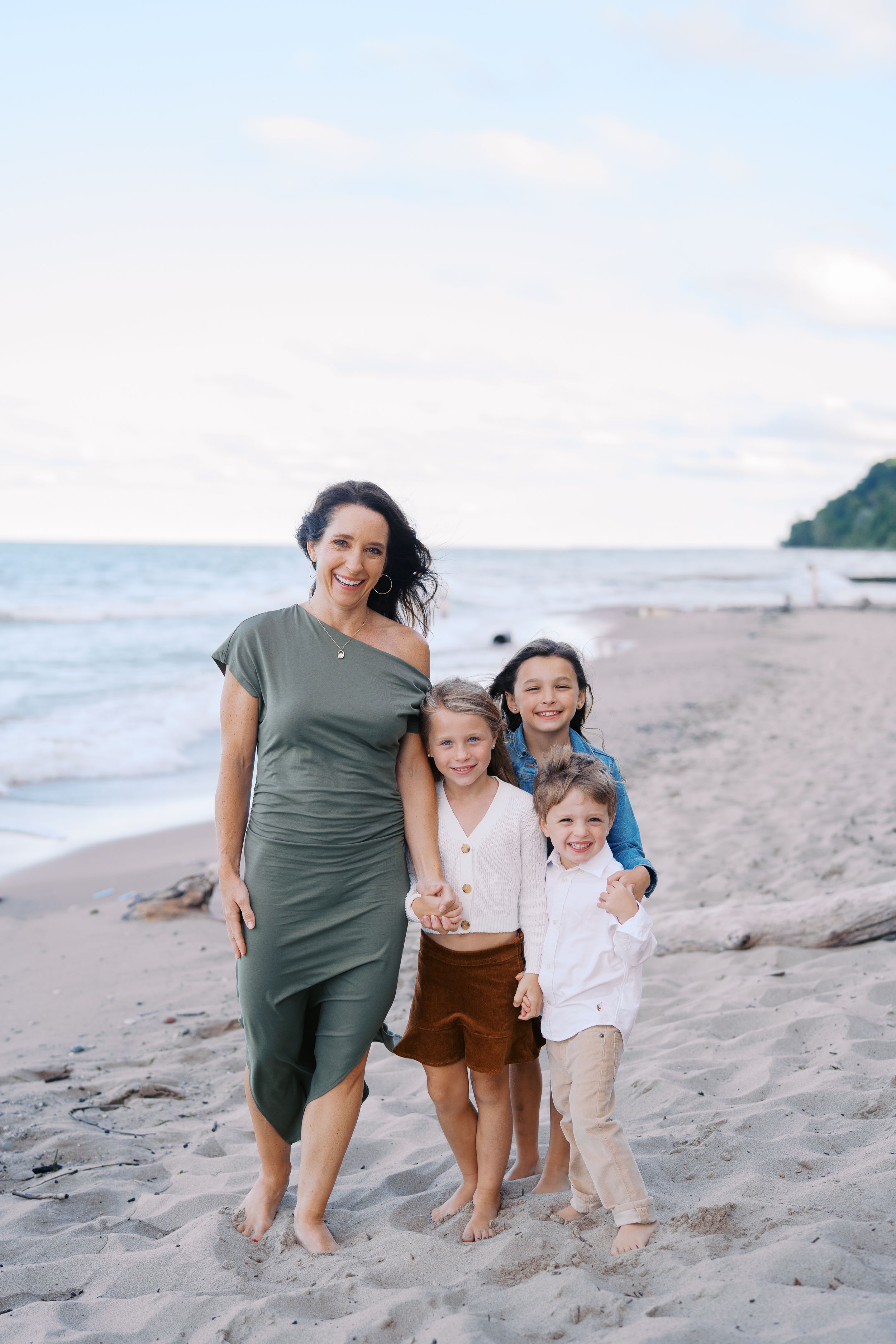 A family group poses together on a sandy beach with ocean waves and cliffs in the background.