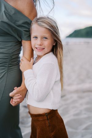 A tender beach moment captured in soft lighting with brown corduroy skirt and cream sweater details.