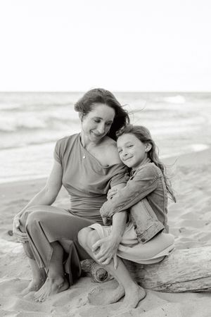 Black and white beach photos show tender moments between parent and child sitting in the sand.